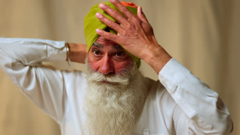 Fotografía-De-Estudio-De-Un-Hombre-Sikh-Mayor-Con-Barba-Atando-Tela-Para-Un-Turbante-Contra-Un-Fondo-Liso,-Filmada-En-Tiempo-Real